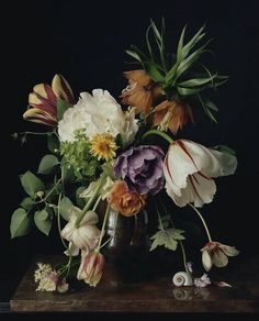 a vase filled with lots of flowers on top of a wooden table in front of a black background