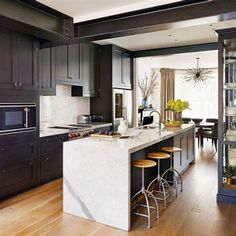 a kitchen with black cabinets and white marble counter tops, an island in the center