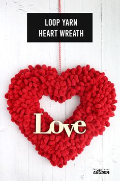 a heart shaped wreath with the word love hanging from it's side on a white wooden background