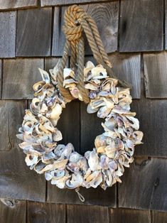 a wreath made out of seashells hangs on a wooden wall next to a rope