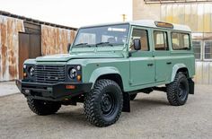 a green land rover vehicle parked in front of an old building with rusted metal doors