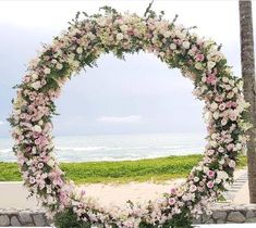 a wedding arch with pink and white flowers in front of the ocean on a cloudy day