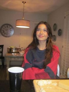 a woman sitting at a table in front of a cup and some food on the counter