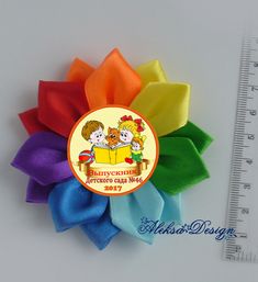 a rainbow colored hair bow with two bears on it and a measuring ruler behind it