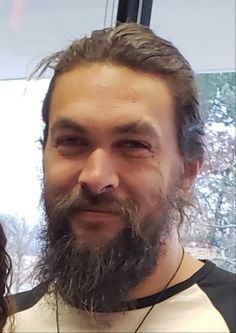 a man with long hair and beard smiling at the camera while standing in front of a window