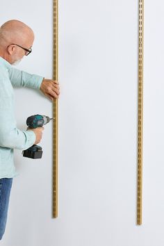 an older man is using a drill to measure the height of a wall with two wooden pegs