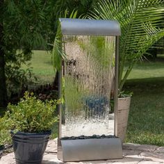 an outdoor fountain with water running down it's sides and plants in the background