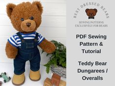 a teddy bear with overalls and striped shirt sitting next to a potted plant