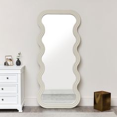 a large white mirror sitting on top of a wooden floor next to a chest of drawers