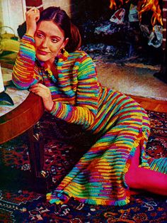 a woman sitting on the floor in front of a piano wearing a colorful sweater and leggings