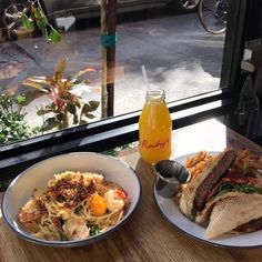 two plates of food on a table next to a bottle of juice and a window