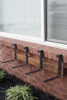 three coat hooks are attached to the side of a brick building with plants in front