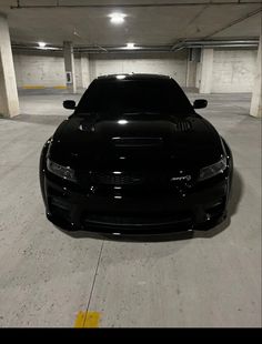 a black sports car is parked in a parking garage with its hood up and lights on