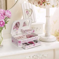 a white dresser topped with pink flowers next to a vase filled with roses and jewelry