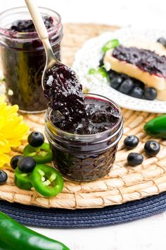 blueberry jam is being spooned into a jar on a plate with green peppers