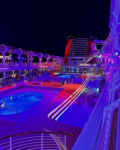 a cruise ship pool at night with blue and red lights on the deck, and water slide