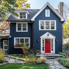 a blue house with white trim and red door in the front yard, surrounded by greenery