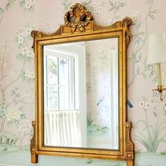 a mirror sitting on top of a dresser next to a wall with flowers painted on it