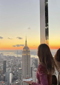 two girls look out at the empire building from top of the rock in new york city