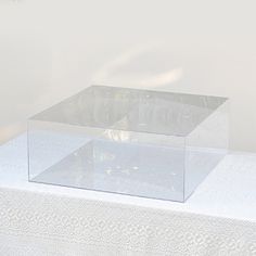 an empty glass box sitting on top of a white tablecloth covered table with flowers