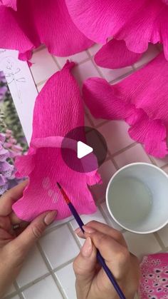 someone is painting pink flowers with watercolors on the paper and using a brush