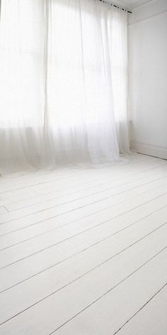 an empty room with white floors and curtains