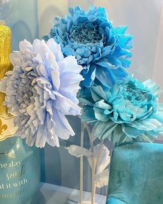 three blue and white flowers sitting on top of a table next to a gold vase