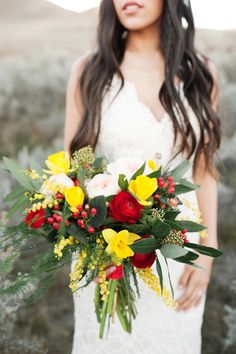 a woman in a wedding dress holding a bridal bouquet with red, yellow and white flowers