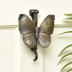 a metal butterfly mounted to the side of a white door next to a green plant