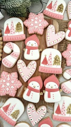 decorated cookies with pink frosting and gold decorations on a wooden board next to pine cones