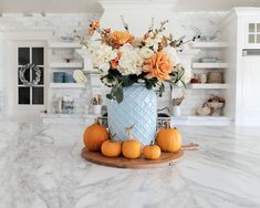 a vase filled with flowers and pumpkins on top of a marble counter in a kitchen