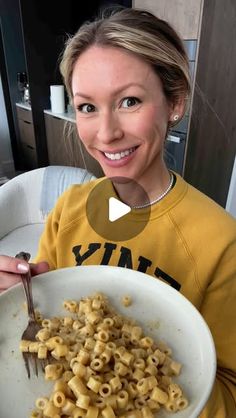 a woman holding a bowl of macaroni and cheese with a fork in it