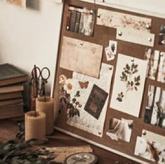 a cork board covered in pictures and papers on top of a wooden table next to candles