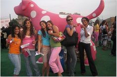 a group of young women standing next to each other in front of a pink cow