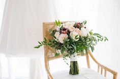 a bouquet of flowers sitting on top of a white table next to a chair in front of a window