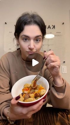 a woman holding a bowl of food with a spoon in her hand and looking at the camera