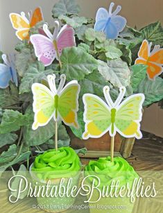 two cupcakes with green frosting and butterflies on them sitting in front of a potted plant