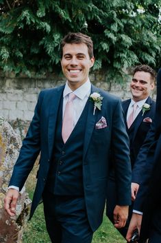 two men in suits and pink ties are walking through the grass with one man holding his hand