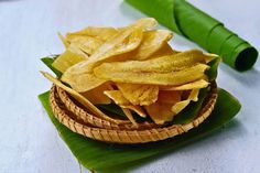 a basket filled with chips sitting on top of a banana leaf next to a green tube