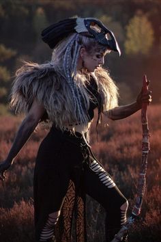 a woman dressed in costume holding a stick and wearing an animal - like headdress