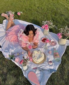 a woman laying on top of a blanket next to a table filled with cakes and flowers