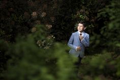 a man in a blue suit and tie is walking through the woods with his hand on his chest