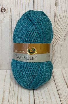 woolspun yarn ball in teal blue on white wooden background with brown stripe