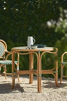 two chairs and a table in the middle of some gravel with plants behind them on either side