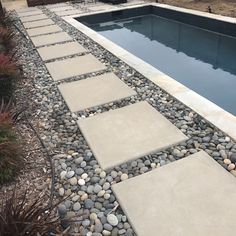 an empty swimming pool surrounded by rocks and gravel with a stone walkway leading up to it