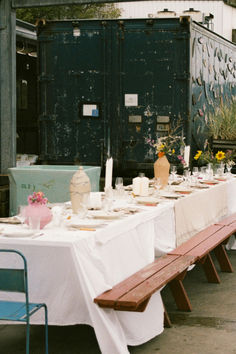 a long table is set up outside with flowers and vases on it, along with other tables