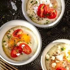 three white bowls filled with food on top of a black table next to gold utensils