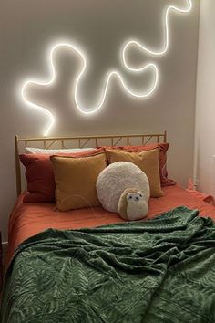 a bed with an orange comforter and two pillows on top of it next to a neon sign