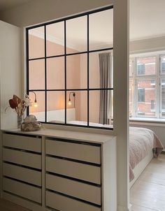 a bedroom with a bed, dresser and large window in the wall next to it