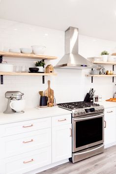 a stove top oven sitting inside of a kitchen next to white cabinets and open shelves